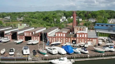 Fly over a river facing an old boat yard with a large brick building - aerial Video stock 161032254