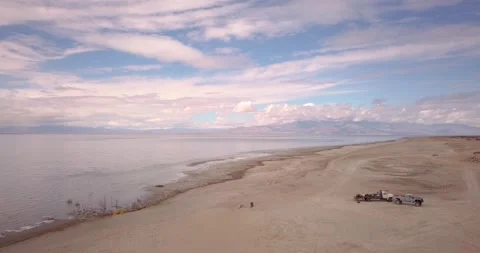 Fly over two pickup trucks parked on the beach at the salton sea Video stock 276854572
