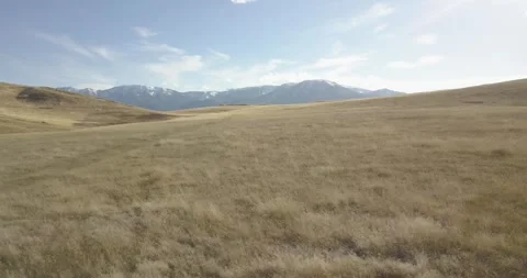 Fly Quickly Backwards over Grassy Fields, Mountain Range Behind, Aerial Drone Stock Footage 281768420