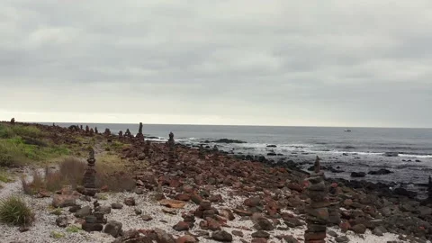 Fly through of multiple stone cairns on the rocky shore of an island by the s Stock Footage 162010350