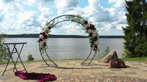 Fly through wedding ceremony circle flower arch to a lake view on a sunny Vídeo Stock 256880262