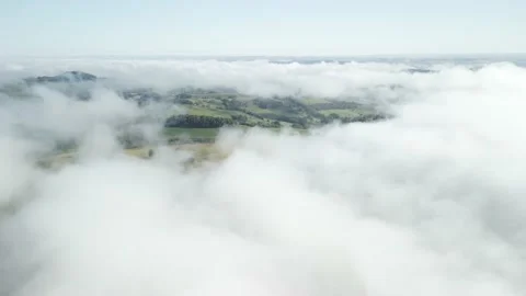 Flying above the clouds over forest and green fields below. Aerial. Stock Footage 233219520