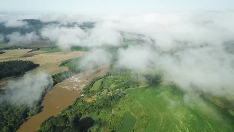 Flying above the clouds over green fields and a river seen through the clouds. Stock Footage 233218284