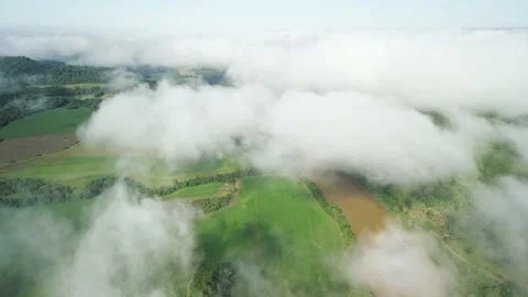 Flying above the clouds over green fields and a river seen through the clouds. Stock Footage 233218407