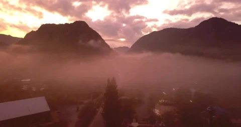 Flying above clouds in sunrise between mountains with a view on a road and town Stock Footage 108469573