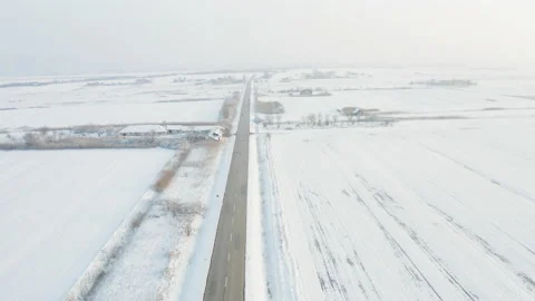 Flying above a large field covered in snow and a road in the middle of it Видео 168530134