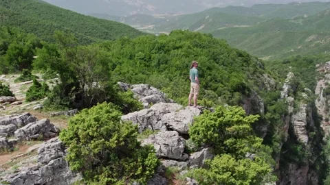 Flying around man at the top of stone cliff. Traveler stands on the edge of Video stock 160041854