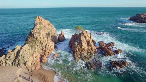 Flying around rocks in the ocean, blue waves crashing on cliff of a rocky coast Stock Footage 165224861