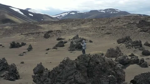 Flying around young man piloting the drone while standing on lava rock Vídeo Stock 149318160