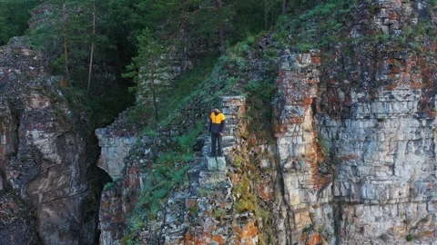 Flying around young man standing on the edge of high rocky cliff Vídeo Stock 247438746