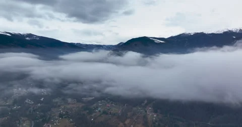 Flying backward through clouds between snow-capped mountains. Aerial Landscape Stock Footage 174439483