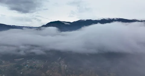 Flying backward through clouds between snow-capped mountains. Aerial Landscape Stock Footage 174440871