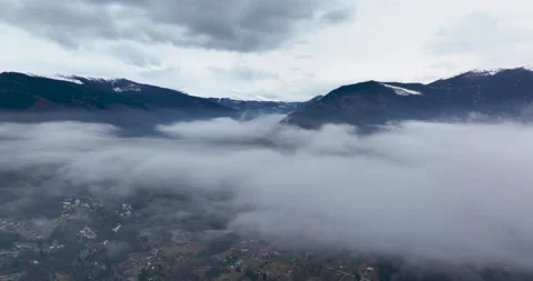 Flying backward through clouds between snow-capped mountains. Aerial Landscape Stock Footage 174458950