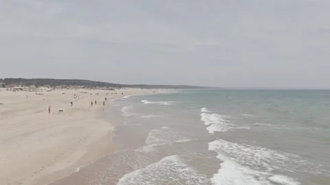 Flying backwards along Costa de Caparica Beach with people on the beach Stock Footage 288706248