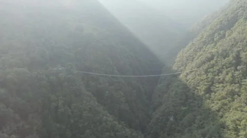 Flying backwards away from mountain suspension bridge with lens flare in camera Stock Footage 282980064