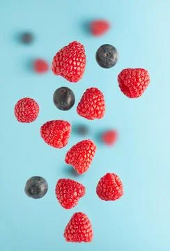 Flying berries over blue table. Falling berries such as raspberry fruits an.. Stock Photos