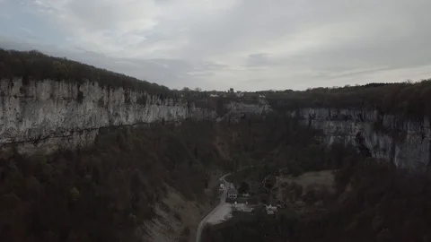 Flying between cliffs and houses on a cloudy weather 1080 ungraded Stock Footage 105953376