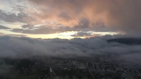 Flying in between small misty town and colorful orange morning clouds Stock Footage 147921409