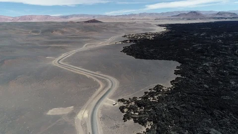 Flying at black bed of lava and desert with road. Descending towards caravan 스톡 동영상 103482334