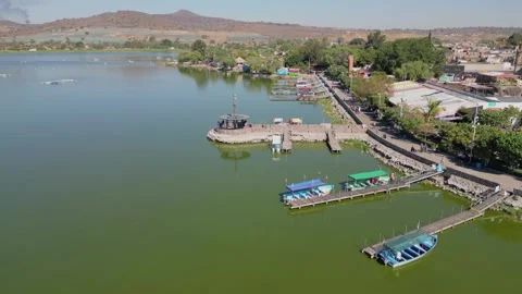 Flying from Cajititlan lagoon toward pier with docks, boats and lakeside walkway Stock Footage 320267661