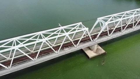 A flying camera flies over a railway bridge a river along which Vietnam Stock Footage 100187860
