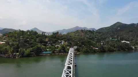 A flying camera flies over a railway bridge a river along which Vietnam Stock-Footage 100187879