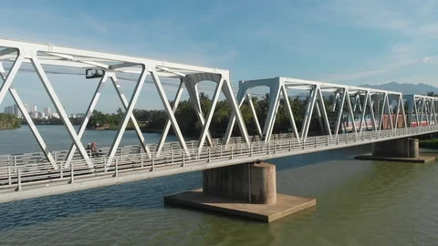 A flying camera flies over a railway bridge stretched across a river along Stock Footage 116113500