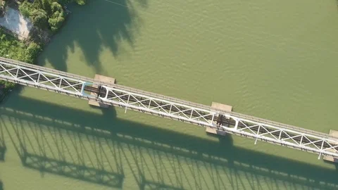 A flying camera flies over a railway bridge stretched across a river along Vídeos de archivo 116113514