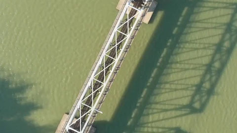 A flying camera flies over a railway bridge stretched across a river along Stock Footage 116113850