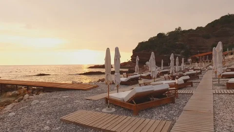 Flying the camera over the double sunbeds on rocky beach. Loungers for two with Stock Footage 129422519