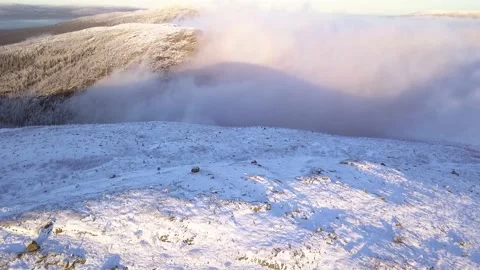 Flying in a clear sky above low clouds over a snow-covered  mountain Stock Footage 143552170