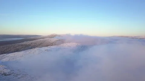 Flying in a clear sky above low clouds over a snow-covered  mountain Stock-Footage 143552347