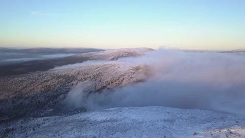Flying in a clear sky above low clouds over a snow-covered  mountain Stock Footage 143575455