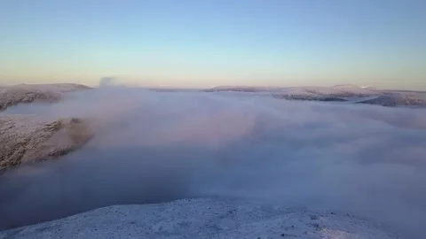 Flying in a clear sky above low clouds over a snow-covered  mountain Stock Footage 143575464