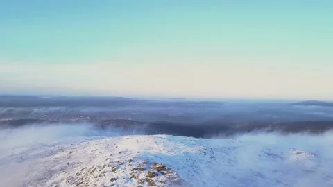Flying in a clear sky above low clouds over a snow-covered  mountain Stock Footage 143575571