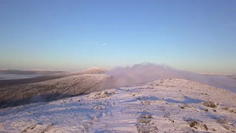 Flying in a clear sky above low clouds over a snow-covered  mountain Stock Footage 143680878