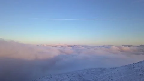 Flying in a clear sky above low clouds over a snow-covered  mountain Stock Footage 143680881