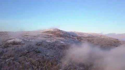 Flying in a clear sky above low clouds over a snow-covered  mountain Stock Footage 143680970