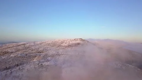Flying in a clear sky above low clouds over a snow-covered  mountain Stock Footage 143681172