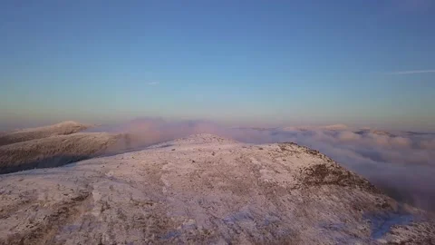 Flying in a clear sky above low clouds over a snow-covered  mountain Stock-Footage 143709994