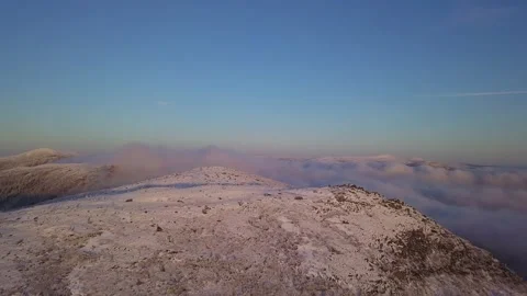 Flying in a clear sky above low clouds over a snow-covered  mountain Stock-Footage 143710331