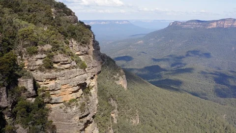 Flying close along a cliff in the mountains towards people standing at a lookout Stock Footage 108529952