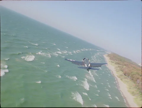 Flying close behind F6F Hellcat over waves and coastline 1990s 35mm film Stock Footage 136384103