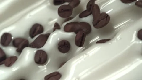 Flying coffee beans mix into flowing milk in slow motion. Close up. Stock Footage 161525932