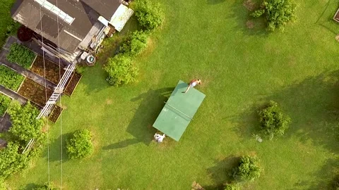 Flying down aerial view of young girl and old man play ping pong in garden Stock Footage 155926971