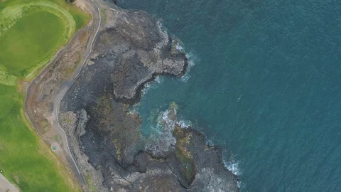 Flying down towards blue ocean, rocky coastline and golf course green field Video stock 90811274