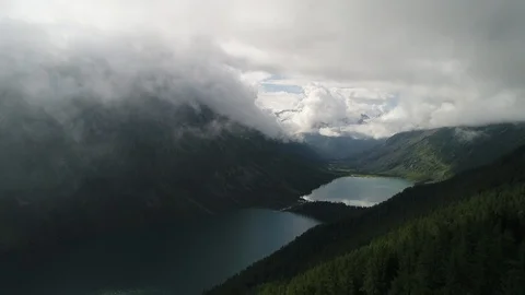 Flying drone to the lake through a cloud over a mountain with cedars Stock Footage 108029926