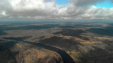 Flying a drone under clouds that cast shadows on the bare autumn forest near the Stock Footage 134697902