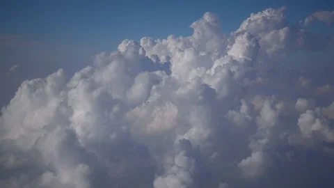 Flying by fluffy white clouds below in the blue sky. Stock Footage