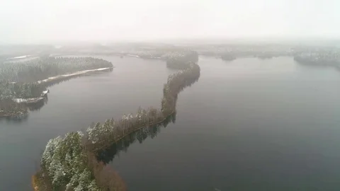 Flying forward over lake with narrow treeline forest covered with light snow Stock Footage 78139129